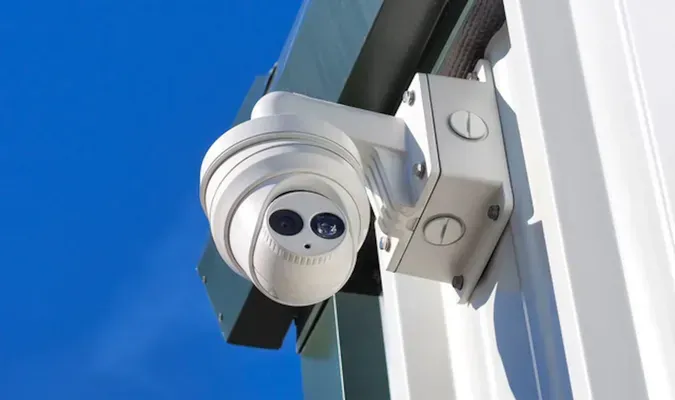 White security camera mounted on a building, against a blue sky.