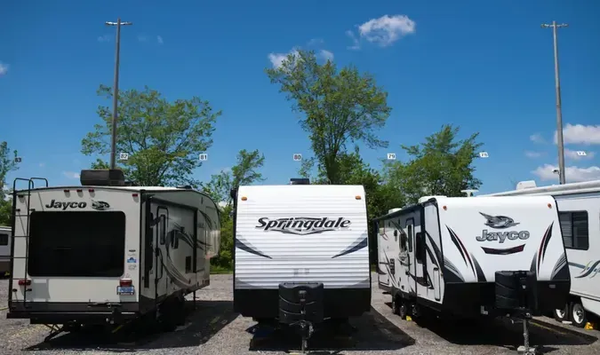 Campers parked outdoors on a sunny day with blue sky and trees.