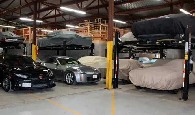 Cars in a garage, some on lifts and covered with car covers.  Building interior with yellow markings and wooden structures.