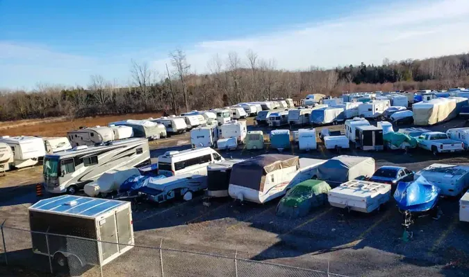 Rows of damaged RVs and trailers in an outdoor lot, many covered in snow or tarps.