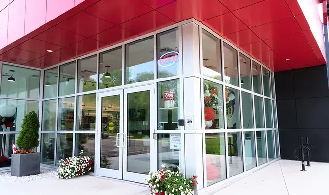 Glass storefront entrance with red awning and potted flowers at the corner of a modern building