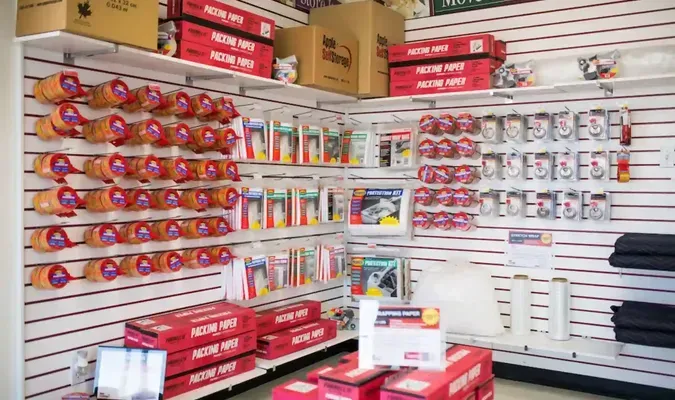 Shelves stocked with packing supplies, including tape rolls and boxes, in a retail store.