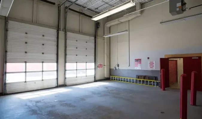 Empty garage interior with closed overhead doors, gray concrete floor, and emergency equipment.