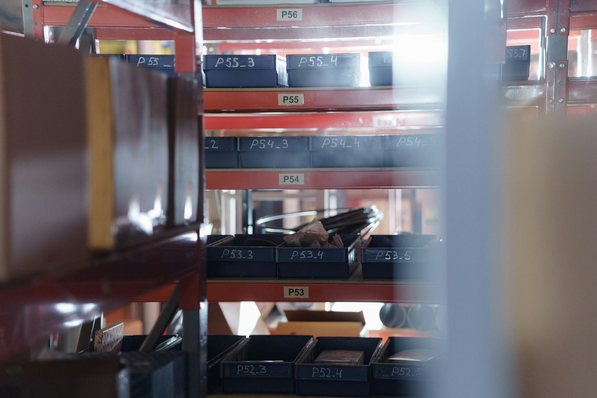 Red warehouse shelves with stacked black trays and blurred foreground racks