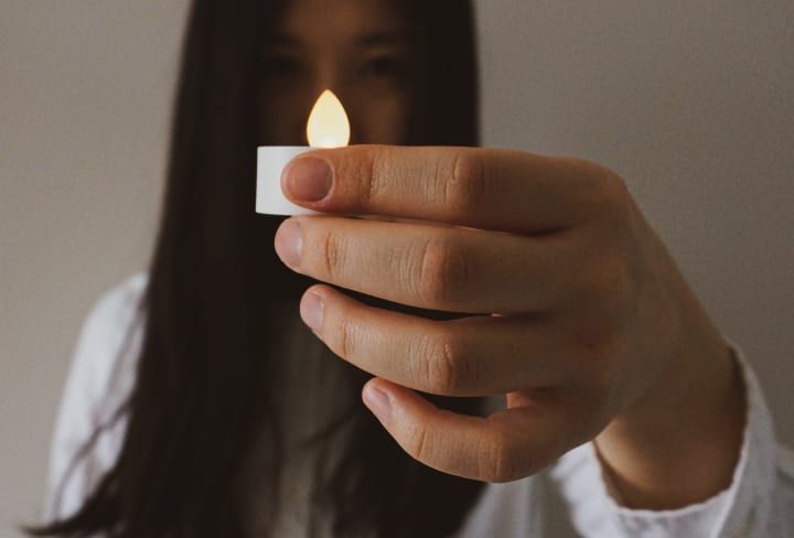 A person holding a small, lit candle, flame visible; focus on hand.