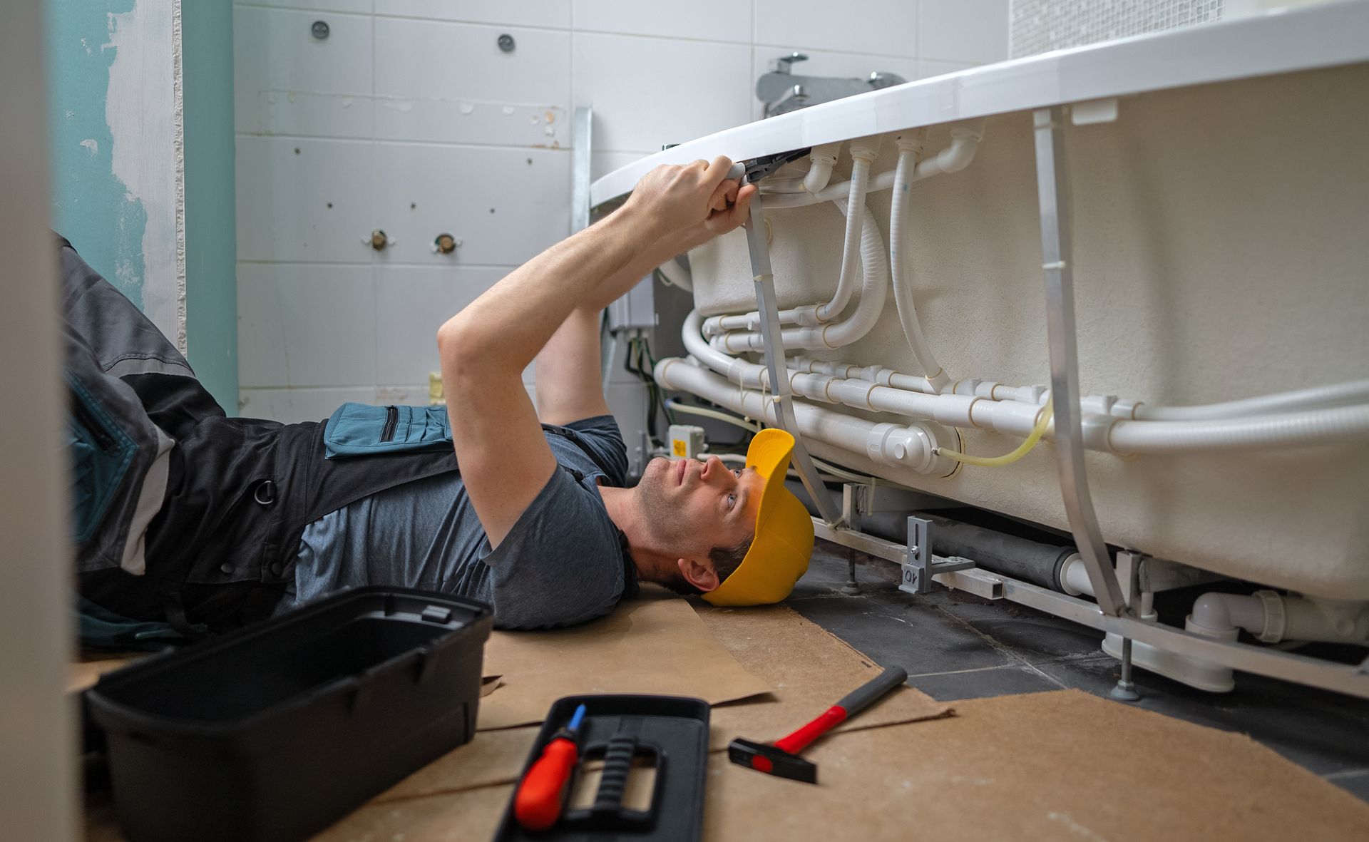 A plumber is fixing a bathtub in a bathroom.
