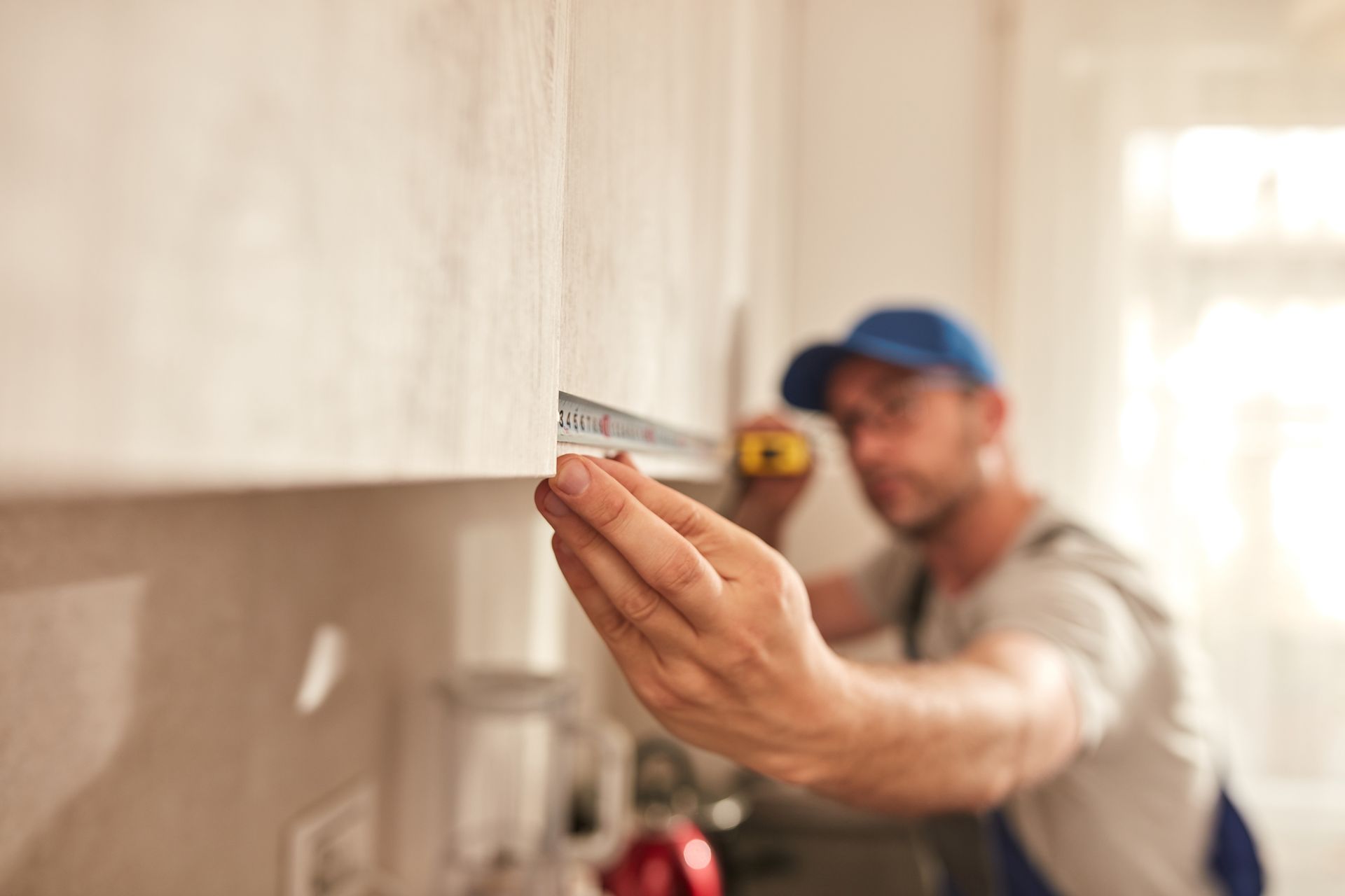 A man is measuring a cabinet with a tape measure in a kitchen.