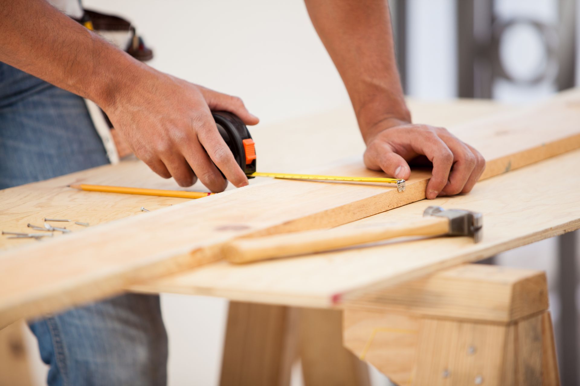 A man is measuring a piece of wood with a tape measure.