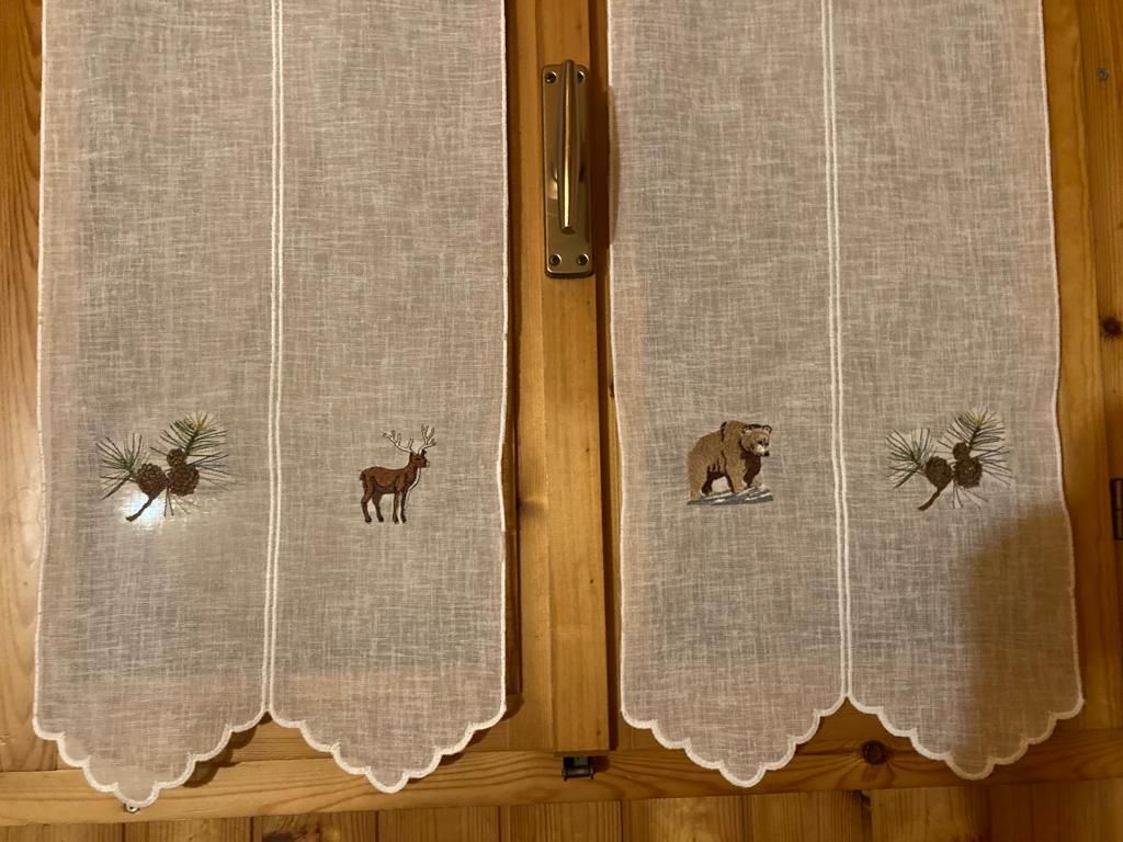 Un paio di tende con animali ricamati sono appese a una finestra di legno.