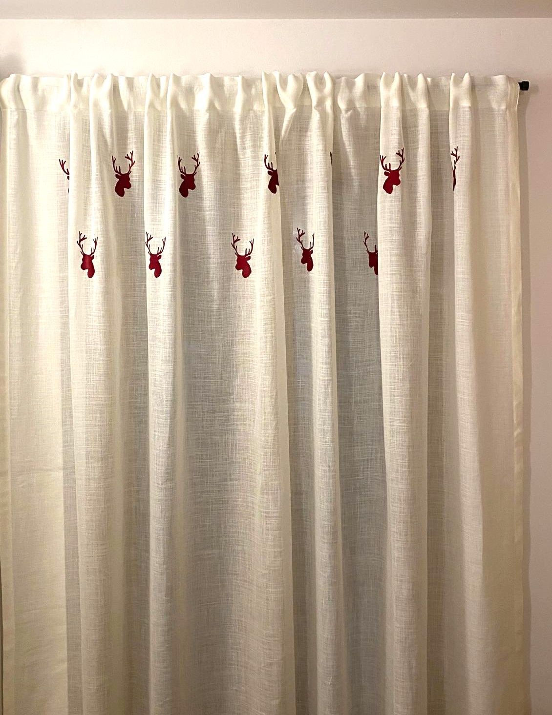 Un paio di tende bianche con dei cervi rossi ricamati.