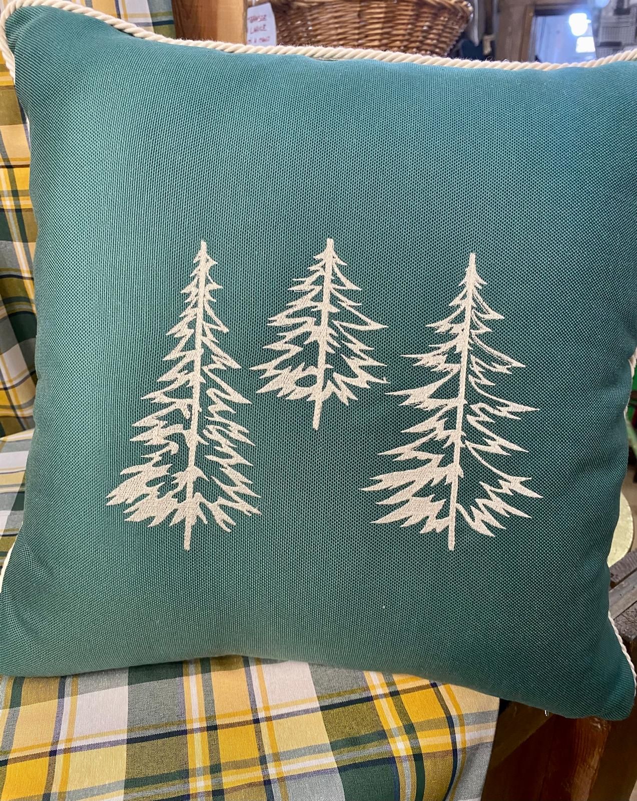 Un cuscino verde con tre alberi ricamati è appoggiato su una sedia.