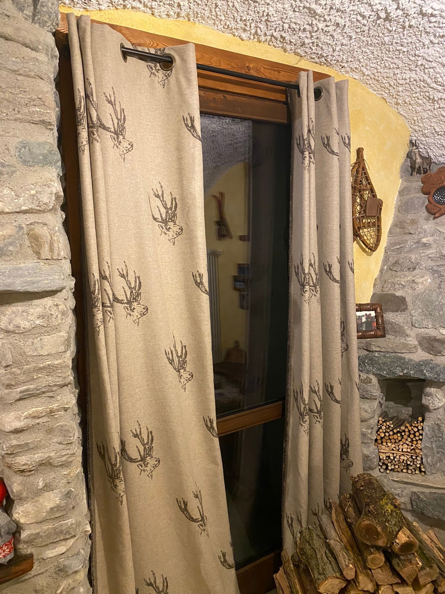 Un paio di tende sono appese a una finestra accanto a una catasta di tronchi.