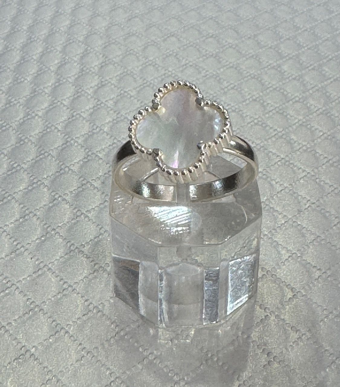 Anillo de trébol de plata con centro de nácar y detalles de diamantes sobre una superficie acolchada.