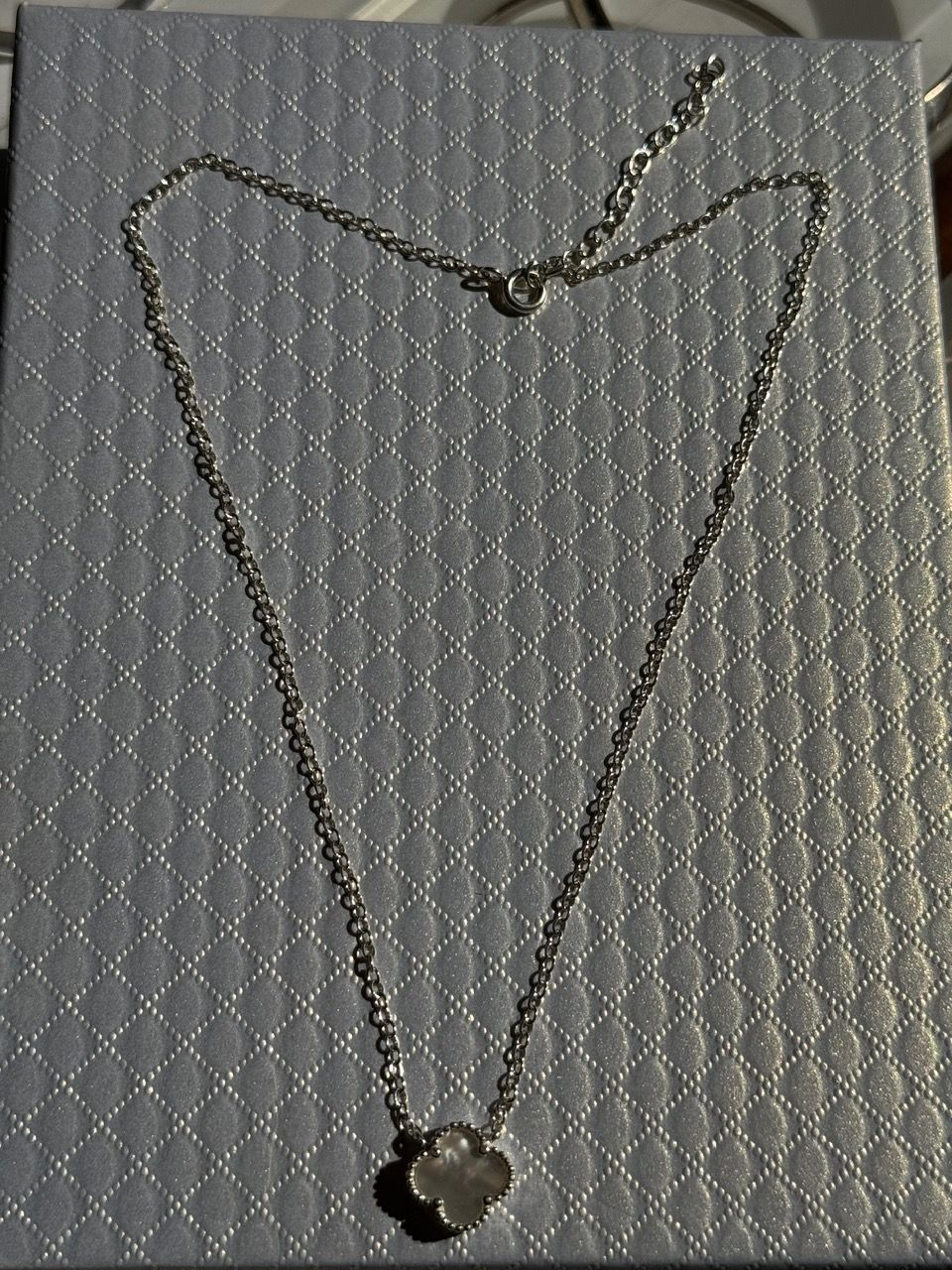 Collar de plata con colgante de trébol sobre una superficie blanca texturizada.