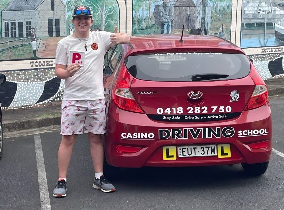 A Man is Standing in Front of a Red Car That Says Casino Driving School — Casino Driving School In Casino, NSW