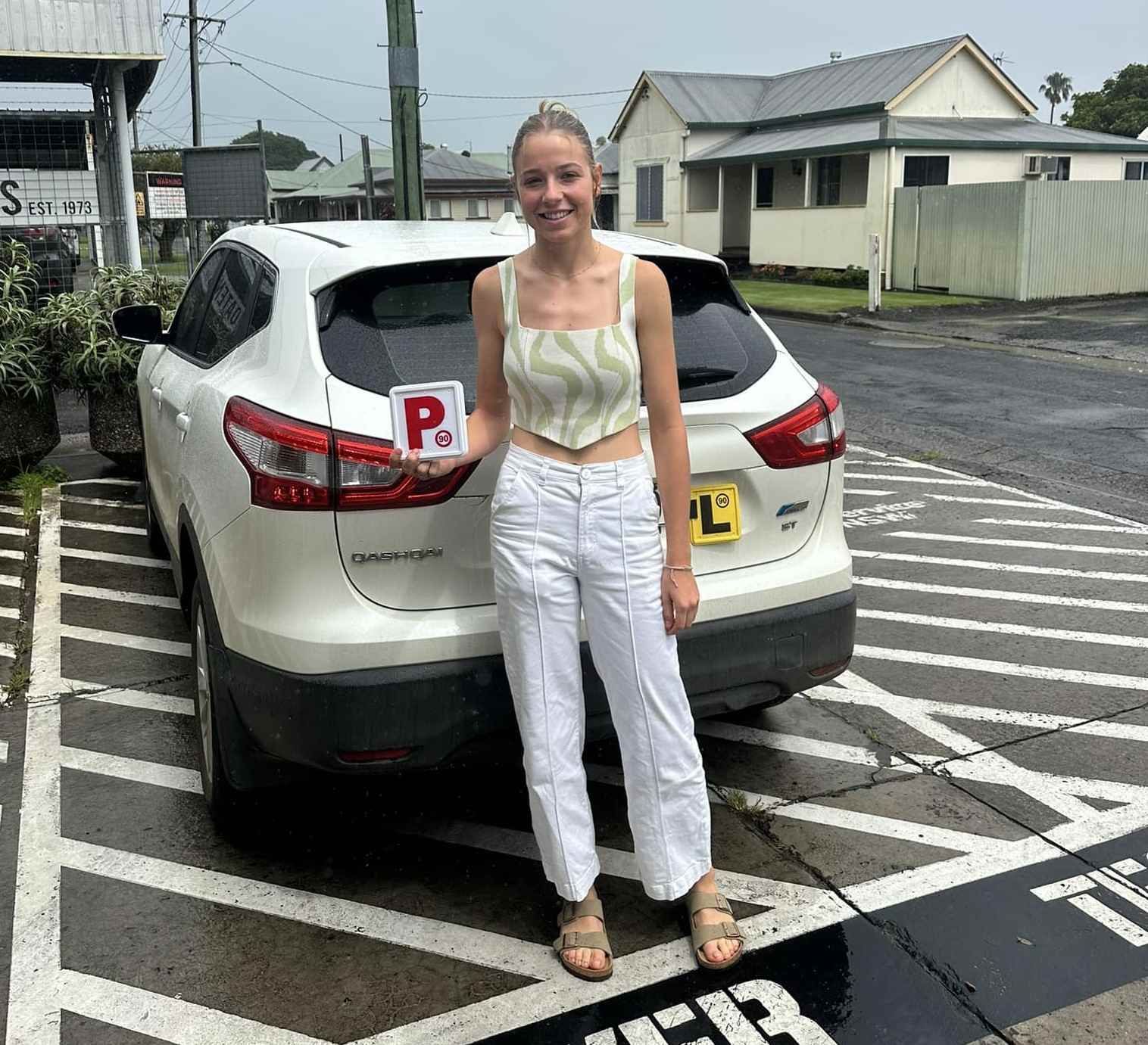 a Woman is Standing in Front of a White Car Holding a License Plate — Casino Driving School In Casino, NSW