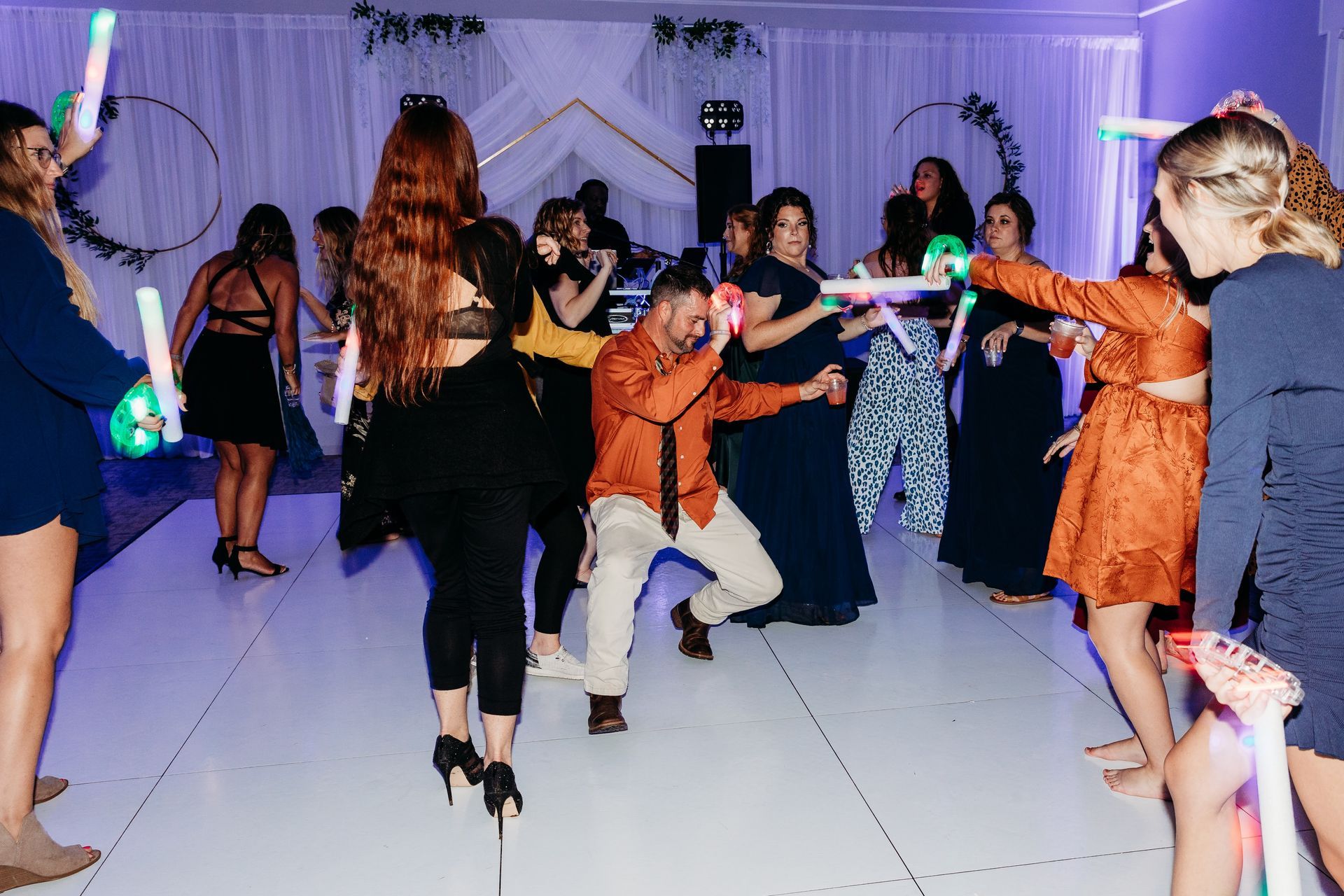People dancing with glowing wands on a white dance floor.