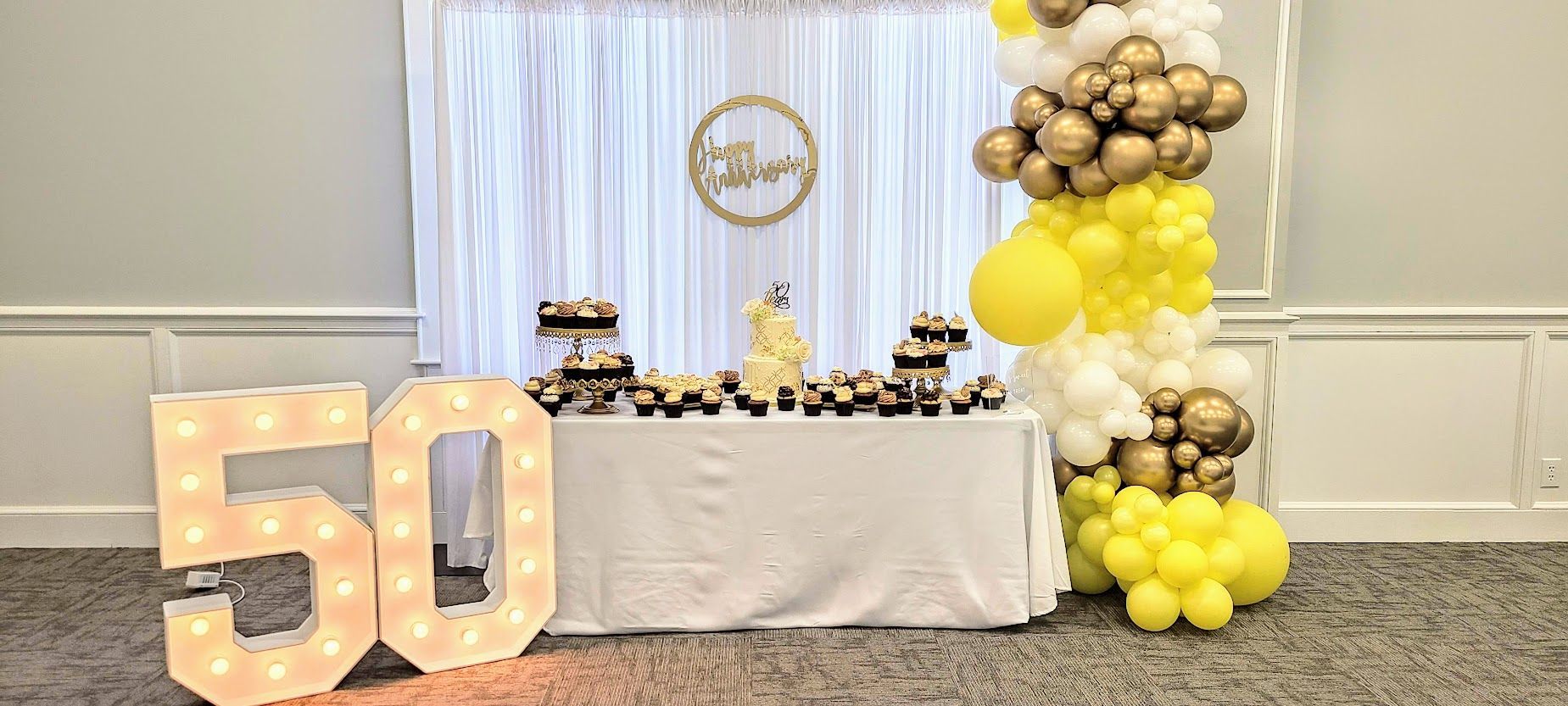 50th birthday party with yellow, gold and white balloons, cake, cupcakes, and illuminated
