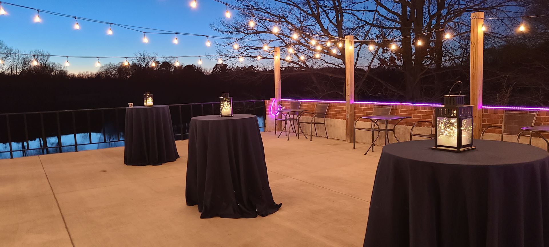 Outdoor evening event with round tables, string lights, and a waterfront view.