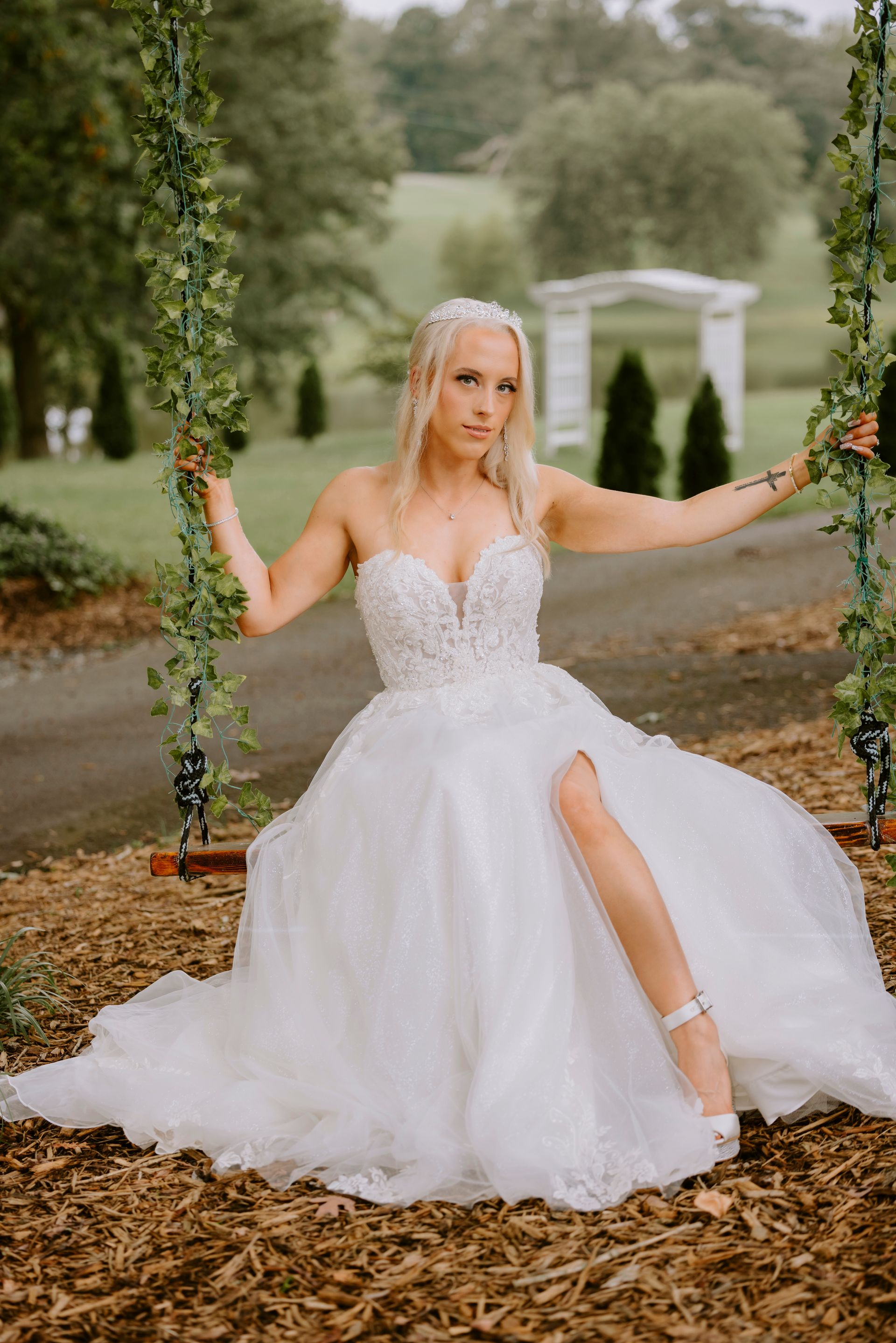 Bride in strapless white gown on swing, trees in background.