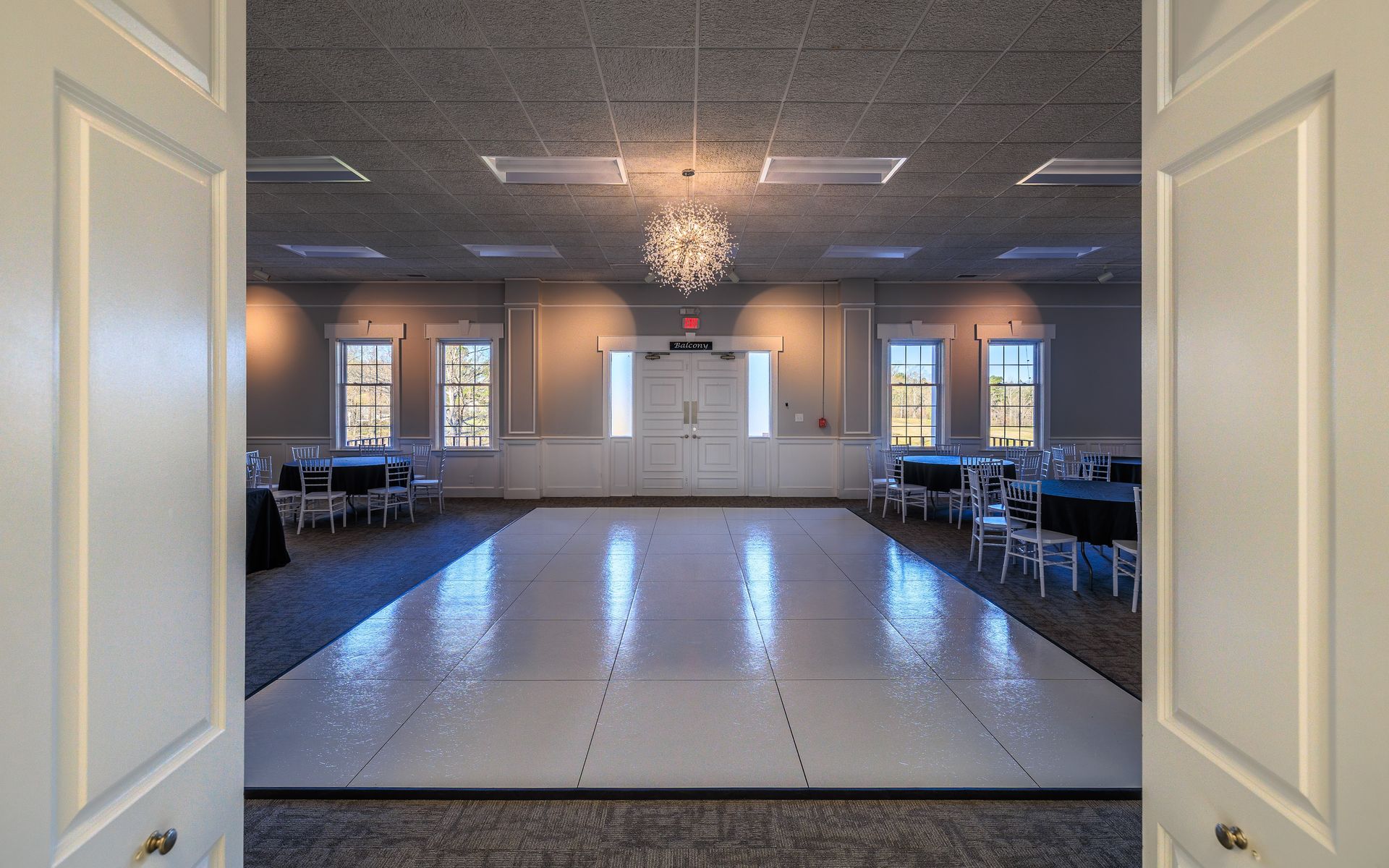 Empty ballroom with a dance floor, set for an event; light fixtures hang from the ceiling.