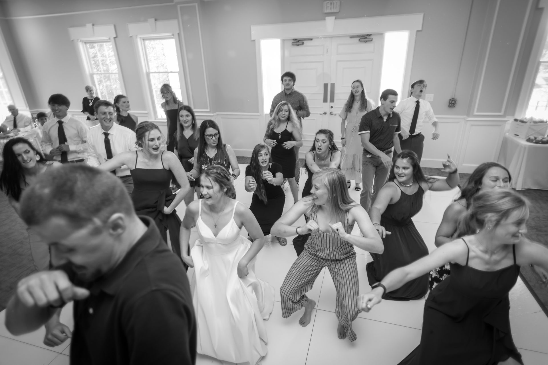 People dancing joyfully at a wedding reception on a dance floor, in a well-lit room.