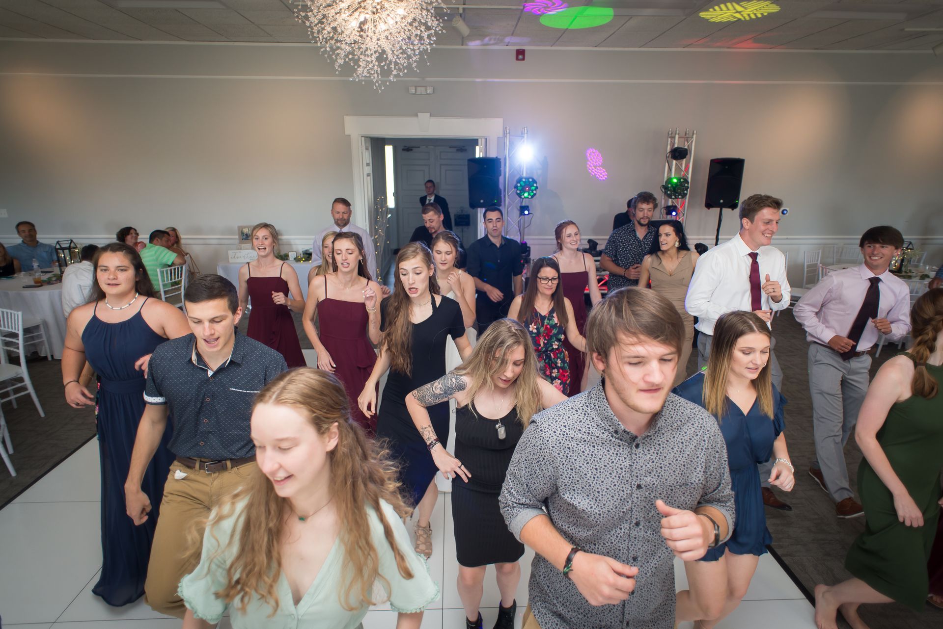 People dancing at a party in a well-lit room with colorful lights.