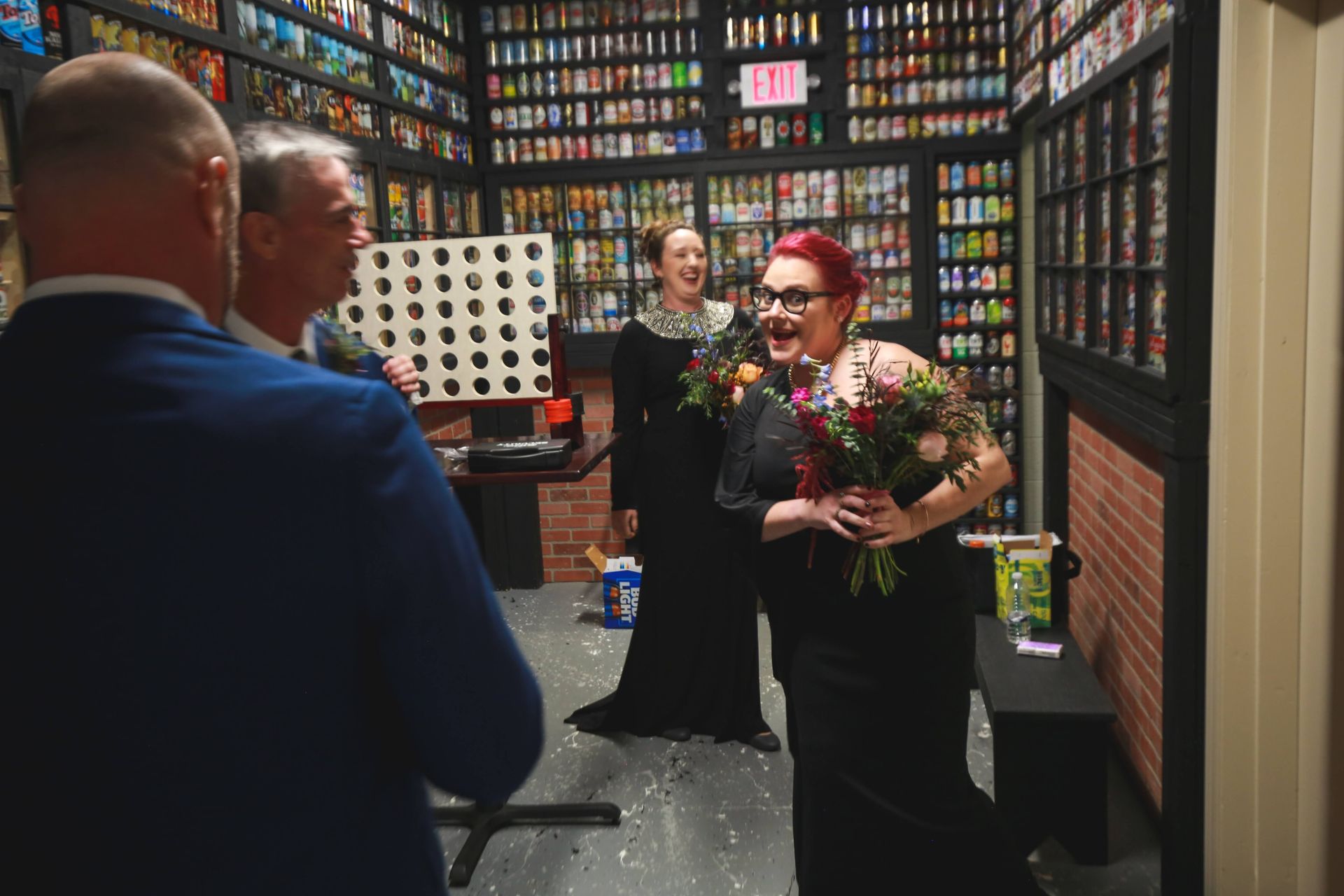 People in room decorated with bottles, one holding flowers, others smiling.