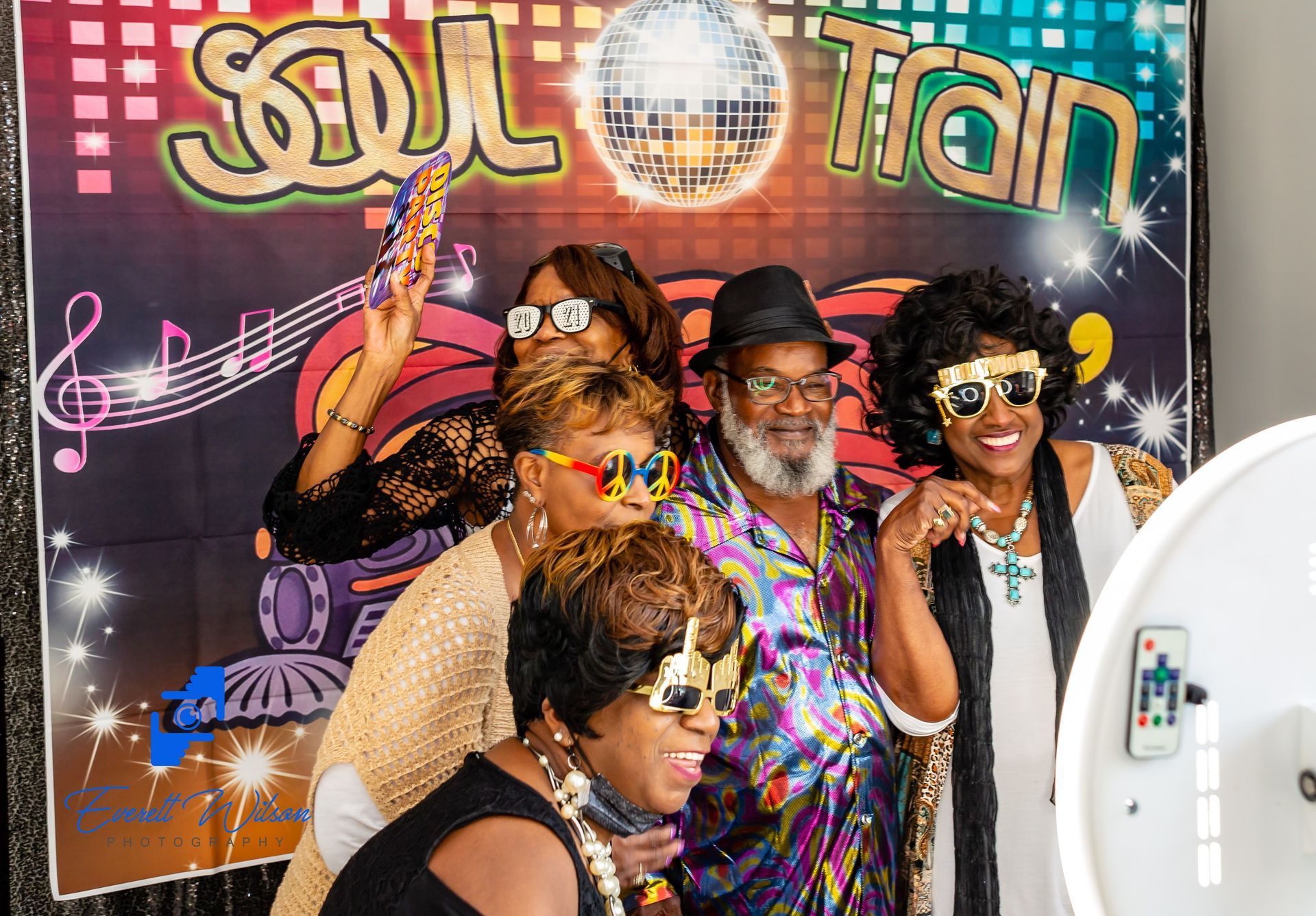 Group posing in front of a Soul Train backdrop with sunglasses and fun props.