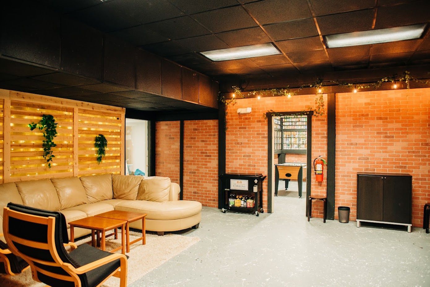 Cozy room with sectional sofa, brick walls, a small table, and a foosball table visible through an open doorway.