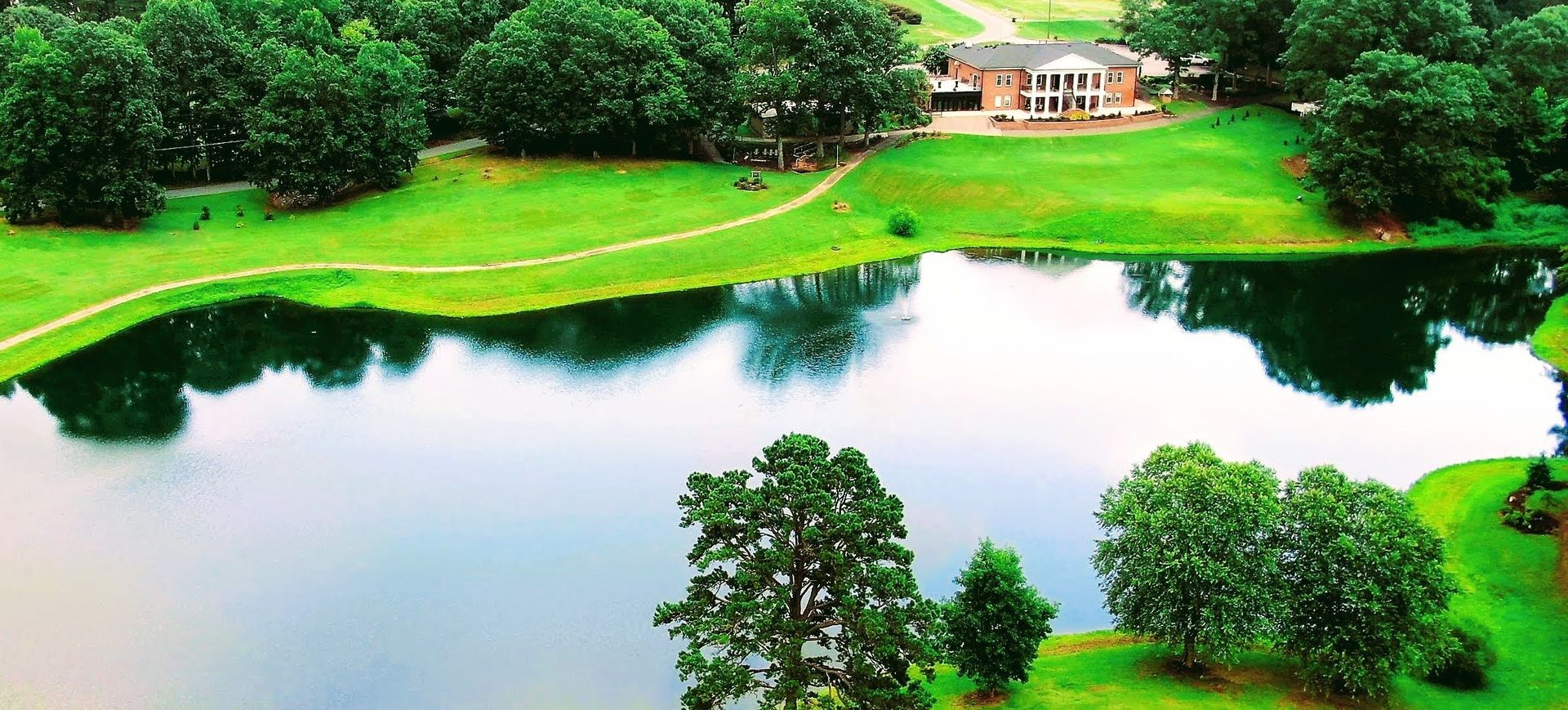 Lush green landscape with a lake, trees, and a house.