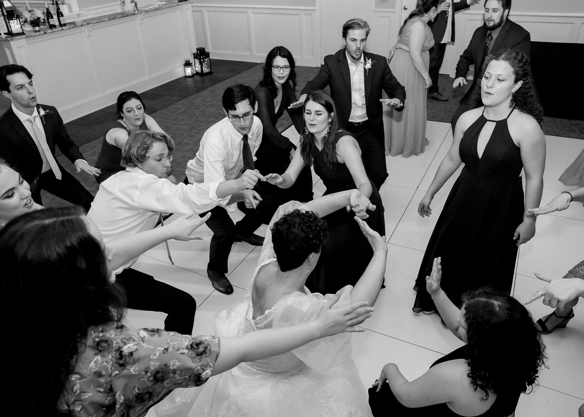 Guests on a dance floor circle around a bride; all are in formal attire and dancing.