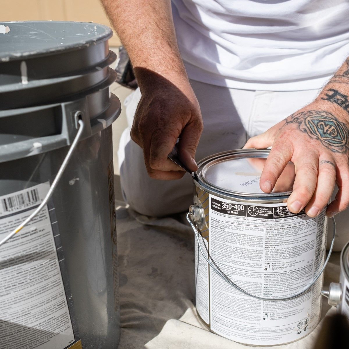A man with a tattoo on his arm is opening a can of paint