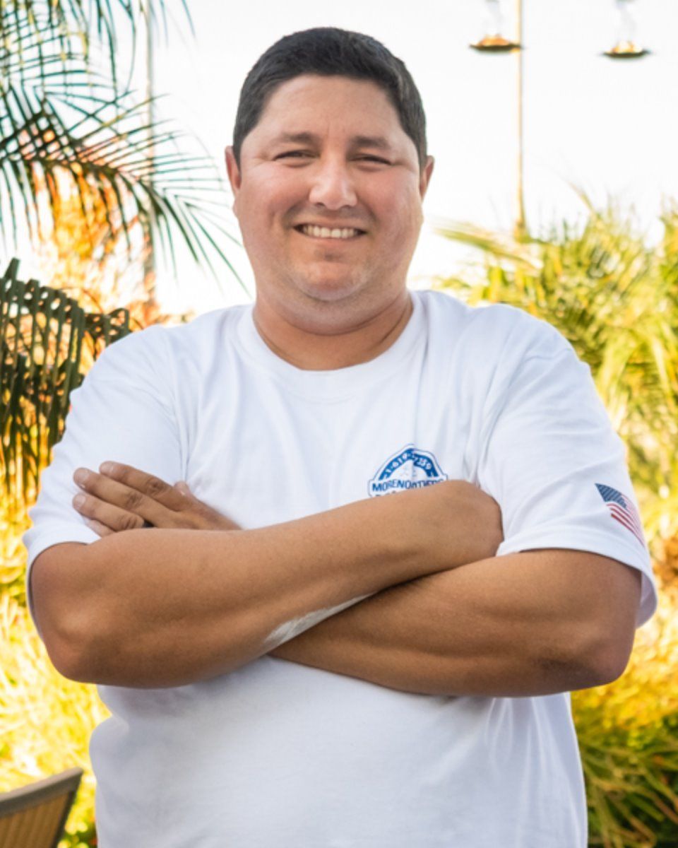 A man in a white shirt has his arms crossed and is smiling
