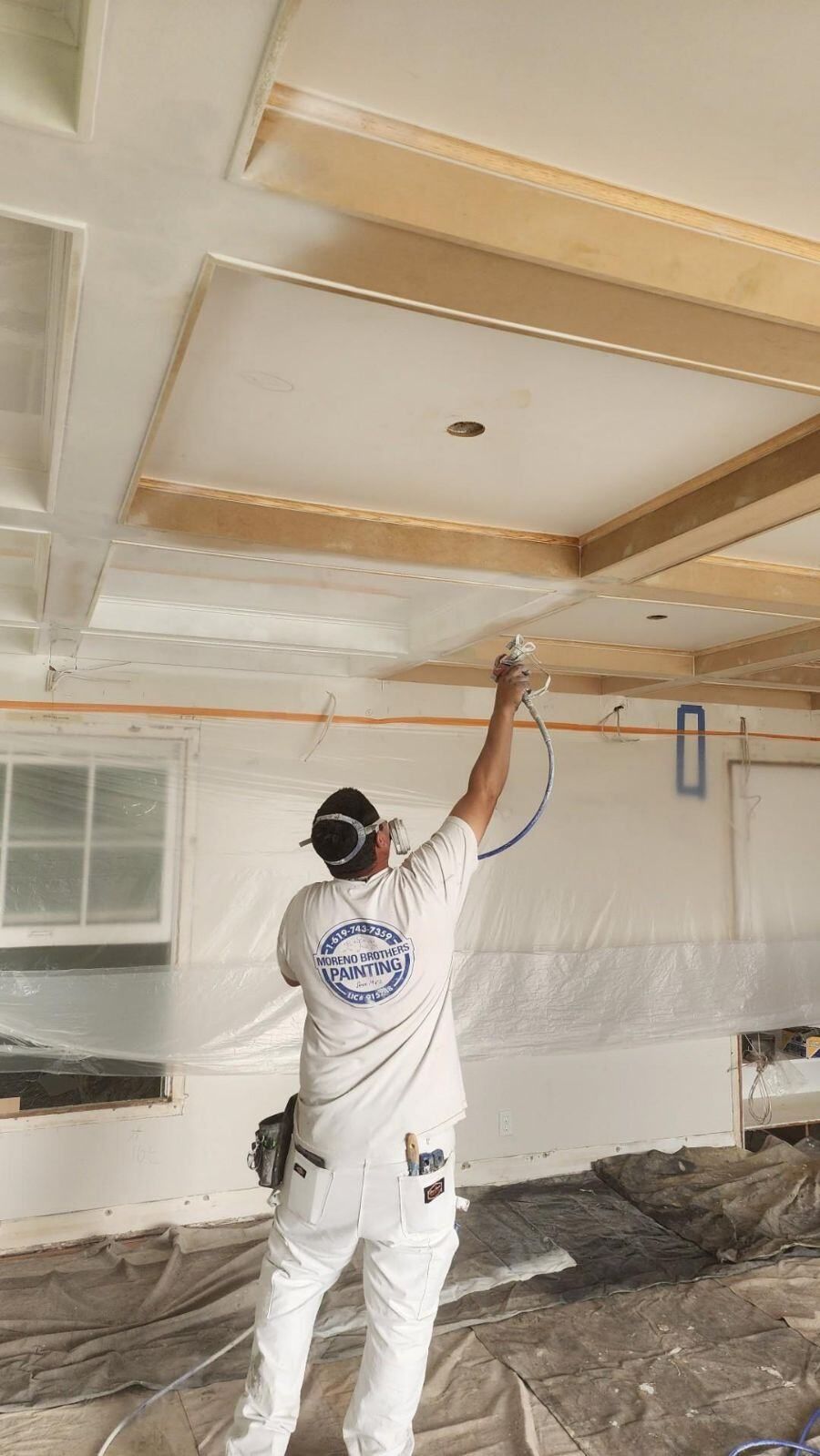 A man is spray painting the ceiling of a room.