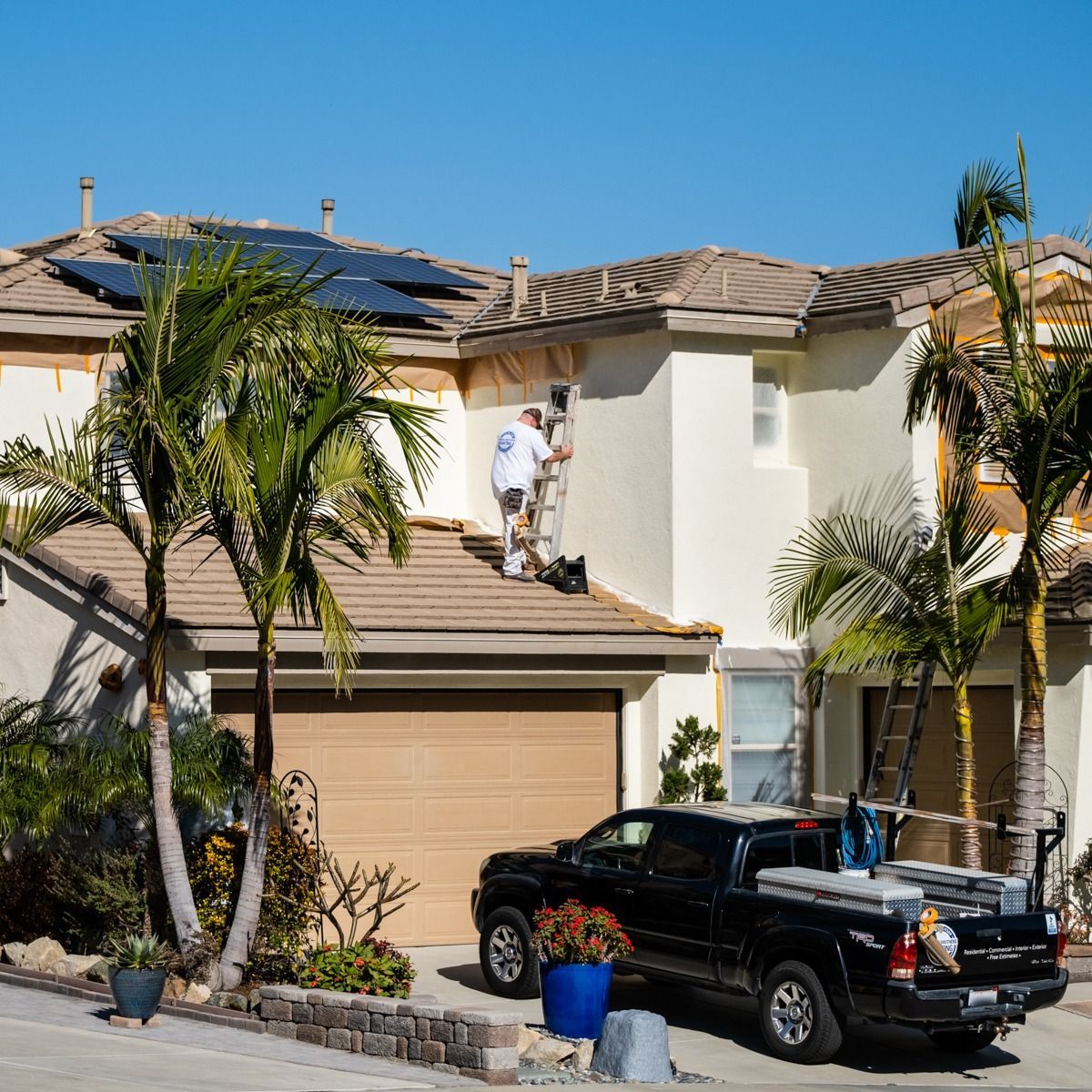 A man is painting the side of a house with a truck parked in front of it.