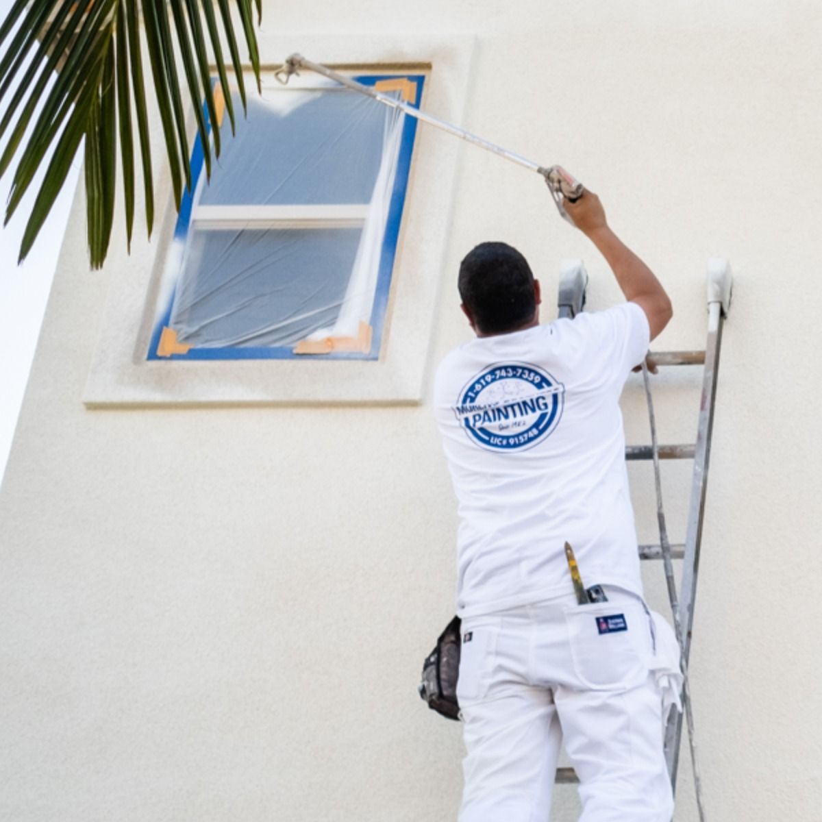 A man on a ladder painting a window with a shirt that says cardinals