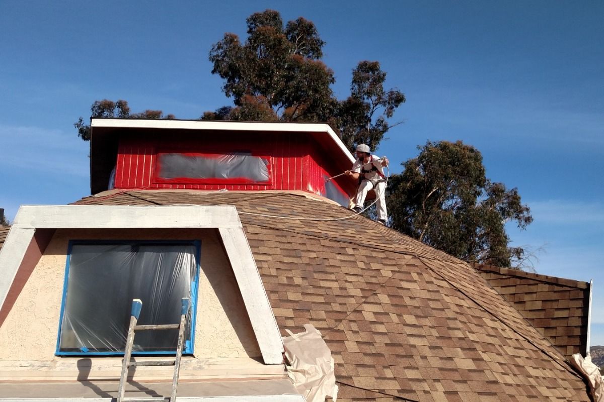 A man is painting the roof of a house with a ladder.