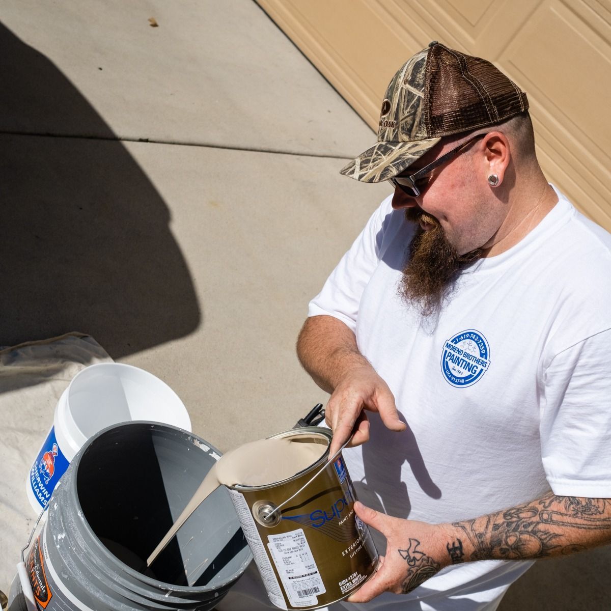 A man in a white shirt is pouring paint into a bucket