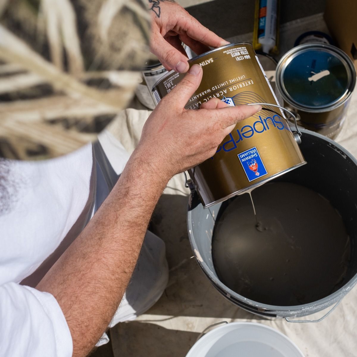 A person is pouring paint from a can that says super