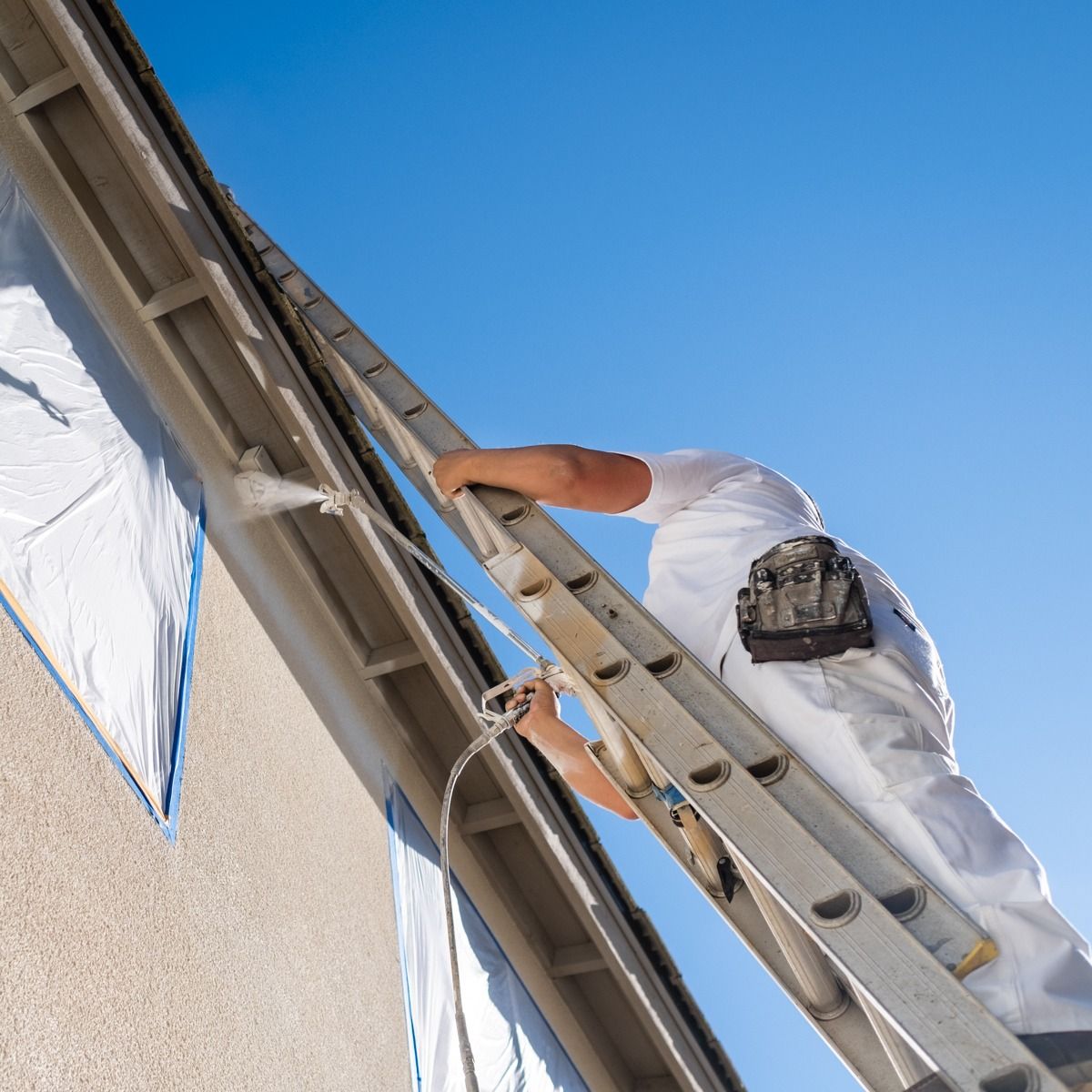 A man on a ladder spraying paint on a building