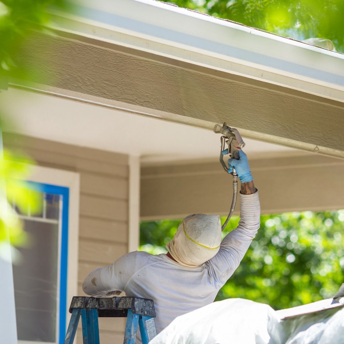 A man is standing on a ladder painting the roof of a house.