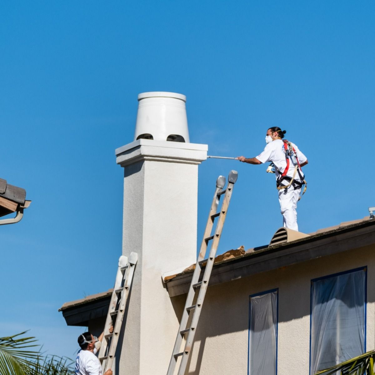 A man paints a chimney on the roof of a house