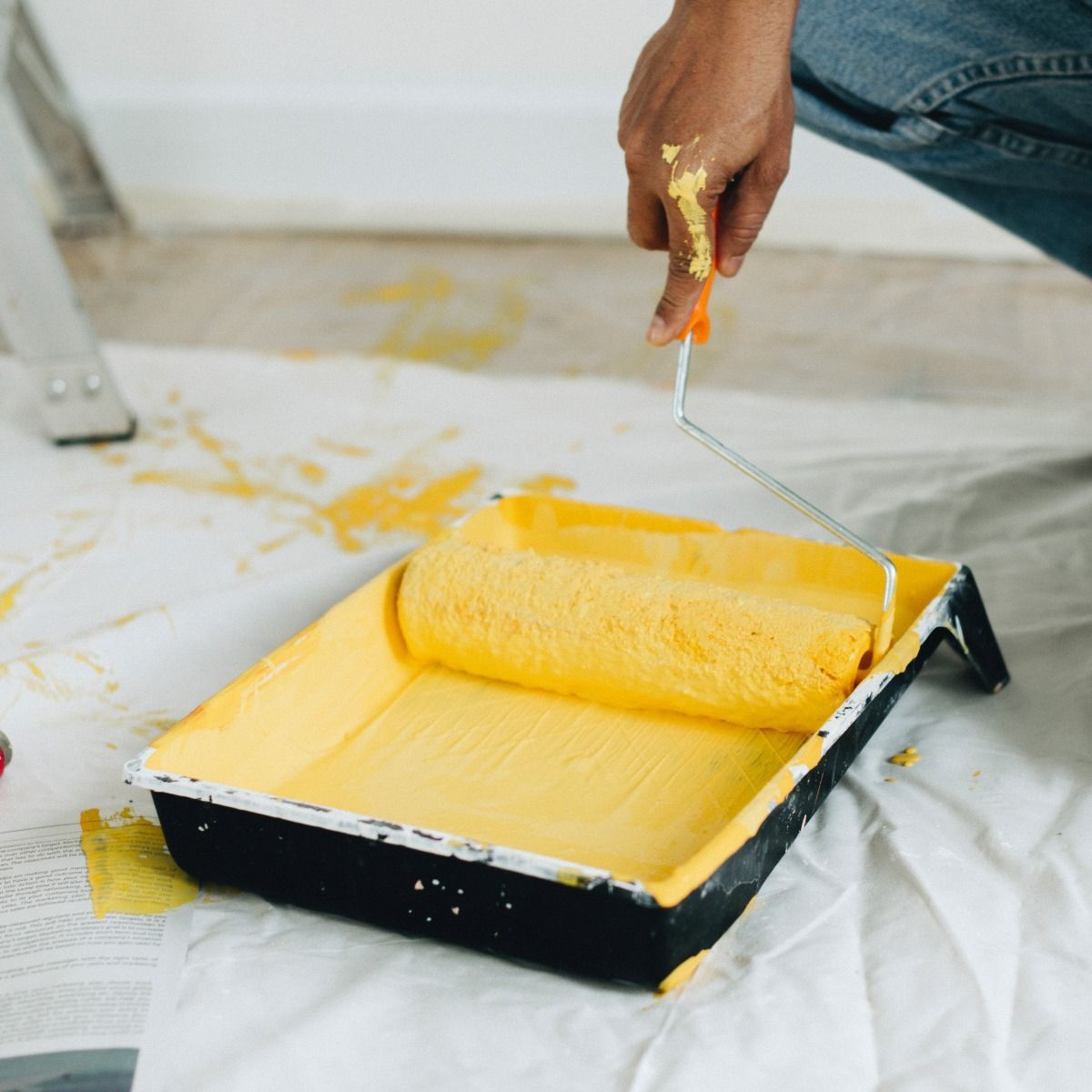 A person is painting a wall with a yellow paint roller