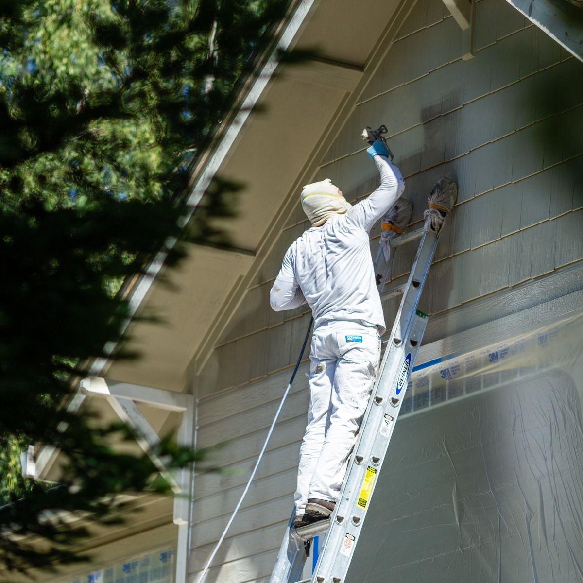 A man is standing on a ladder painting a house.