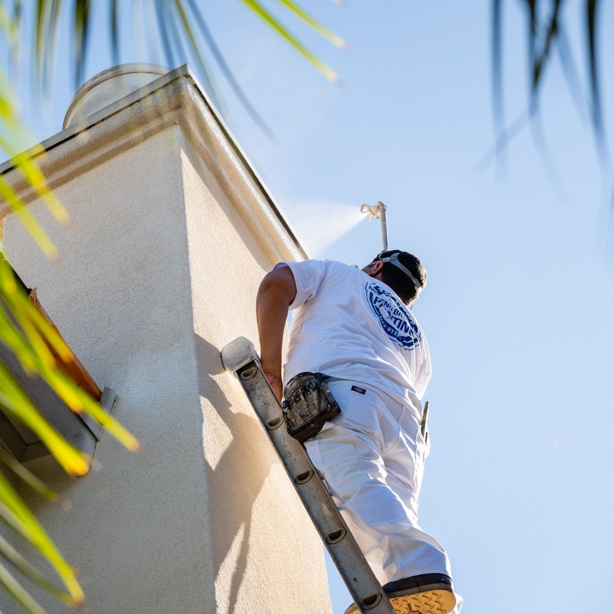 A man on a ladder spraying paint on a building