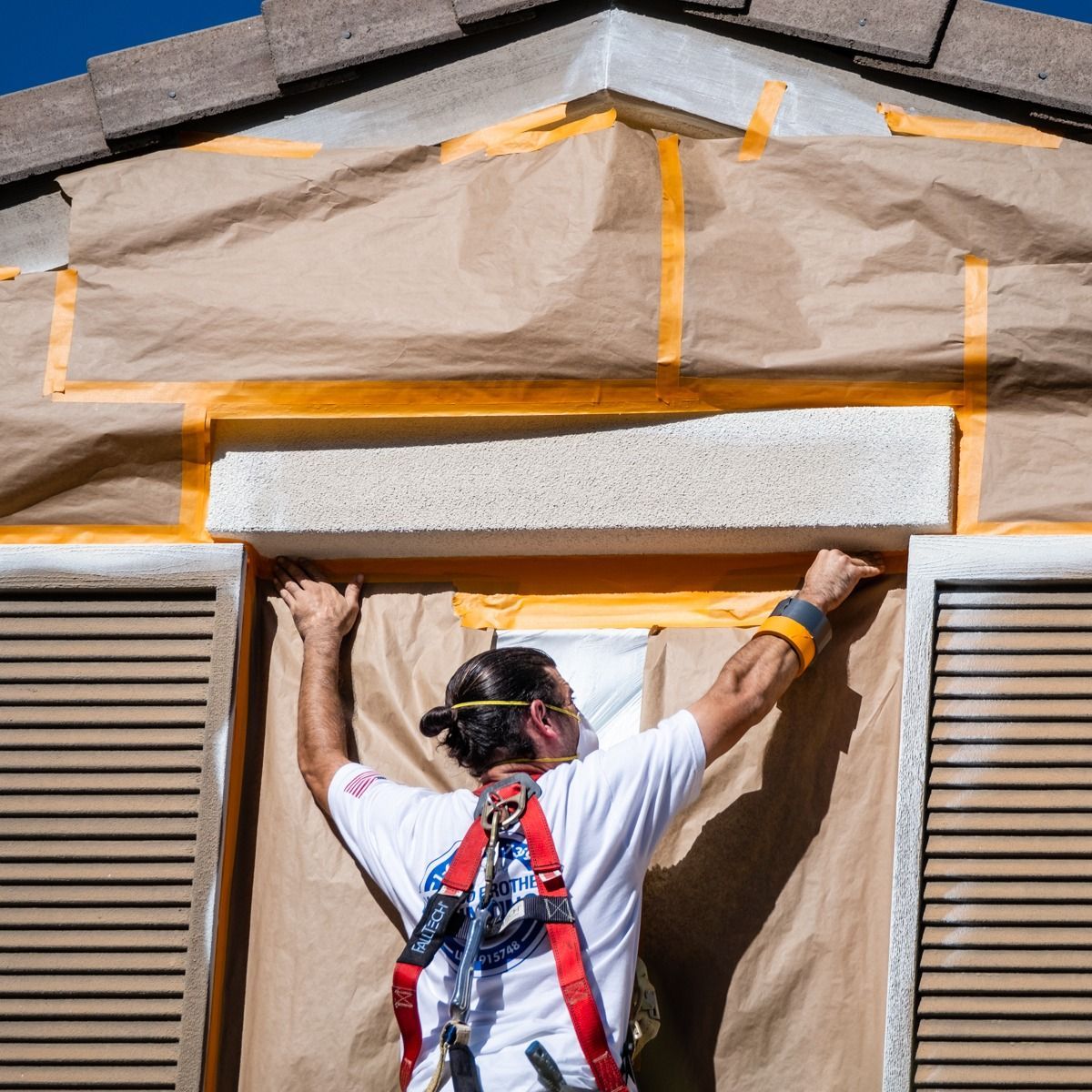 A man wearing a safety harness is working on a window