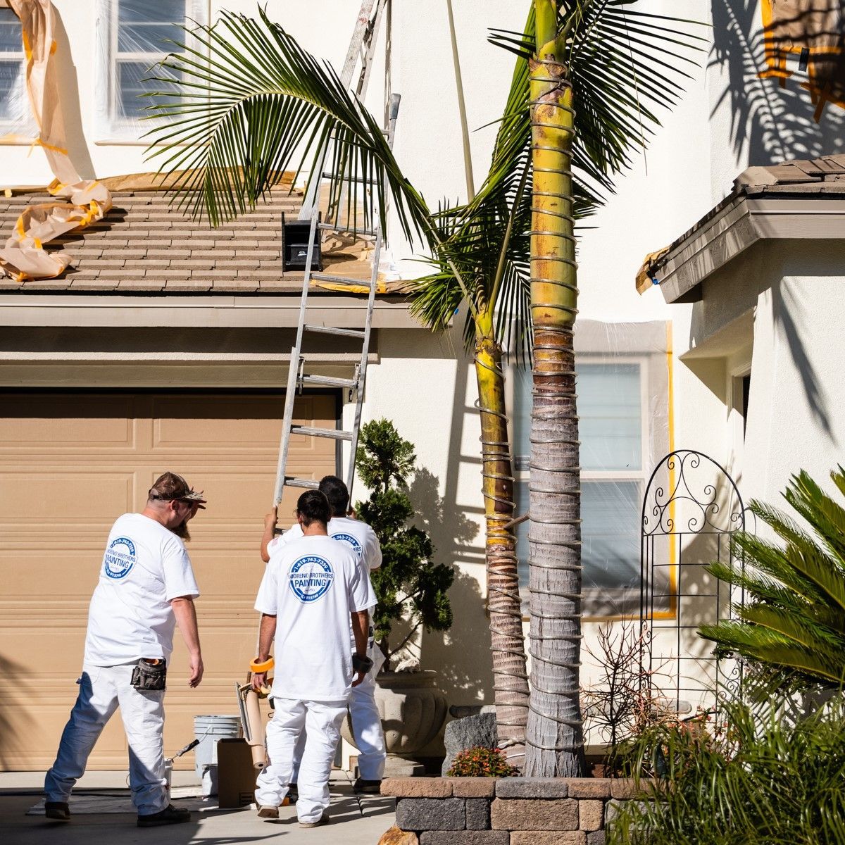 A group of men are painting a house with palm trees in the background.