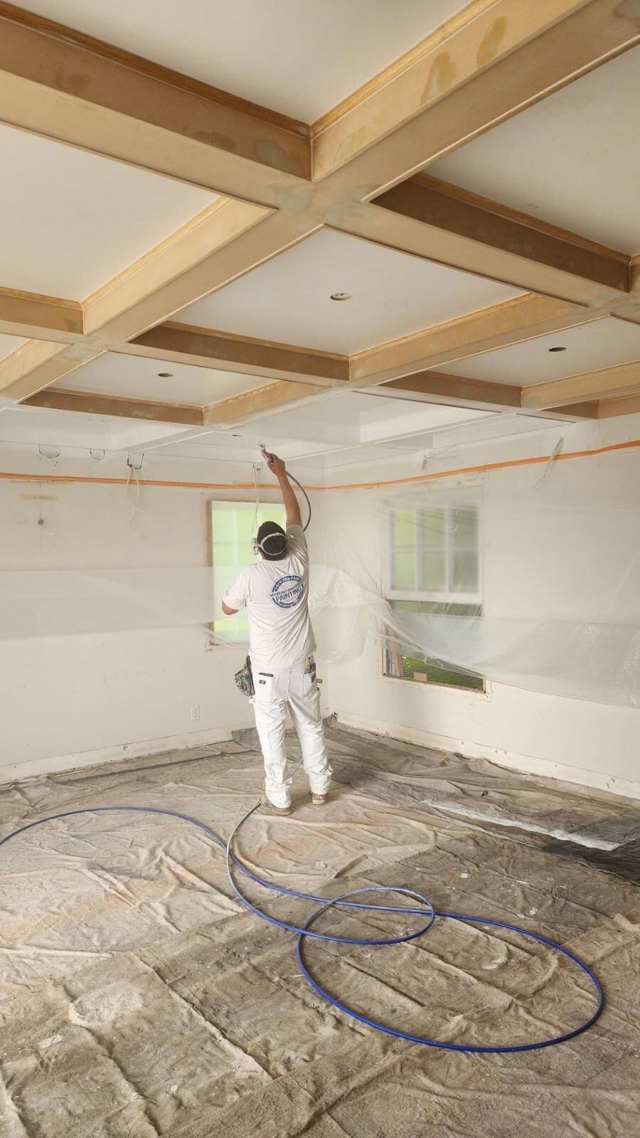 A man is painting the ceiling of a room with a sprayer.