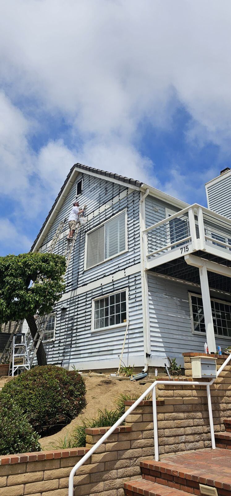 A man is standing on a ladder painting the roof of a house.
